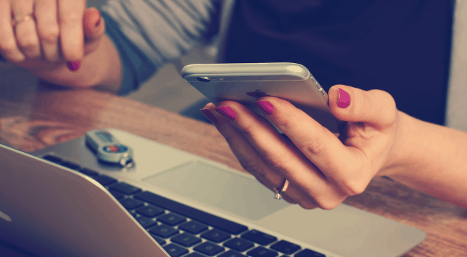 Multitasking workers hands in front of keyboard holding an iPhone with USB drive nearby